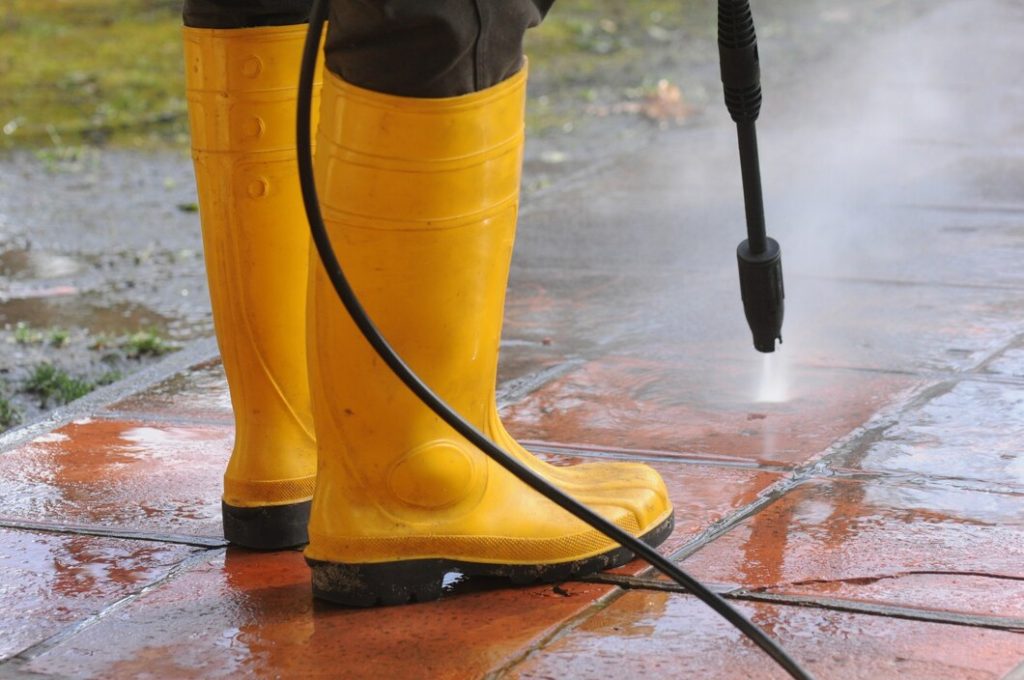 person wearing yellow rubber boots with high pressure water nozzle cleaning dirt tiles 181624 23652