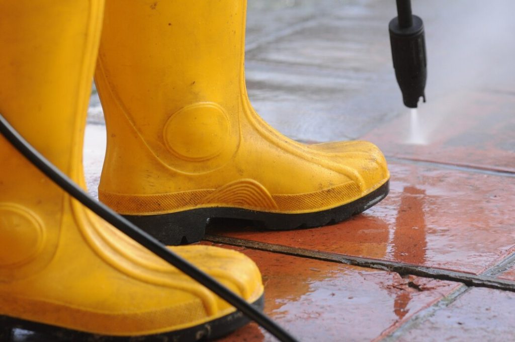 person wearing yellow rubber boots with high pressure water nozzle cleaning dirt tiles 181624 24808